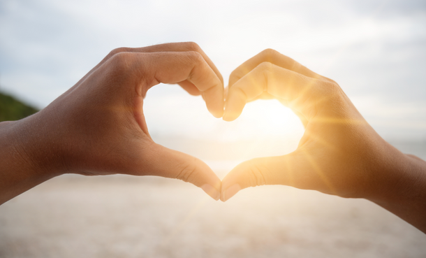 Hands making a heartshape with sun in background