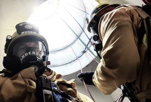 2 firefighters with SCBAs in a confined space hole