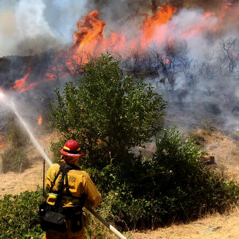 Firefighter sprays water onto active brush fire