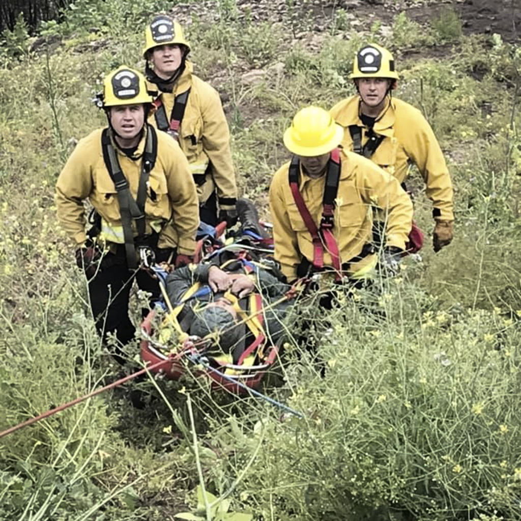 firefighters carry a victim in a litter up a hill