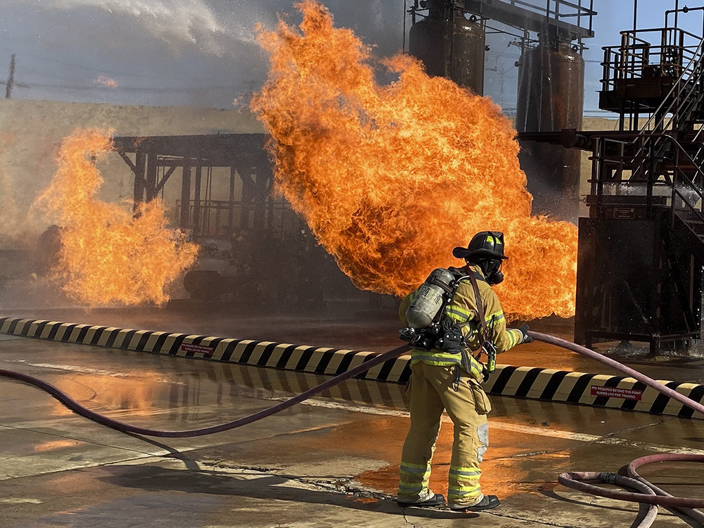 Firefighter flakes hose with refinery fire in background